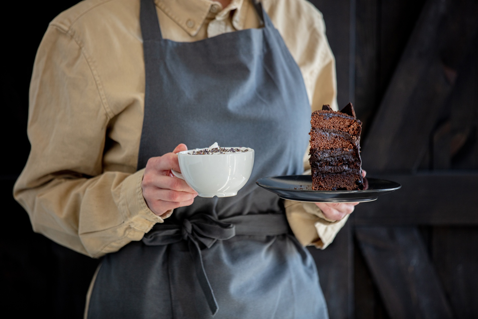 woman in an apron holds cappuccino and chocolate cake