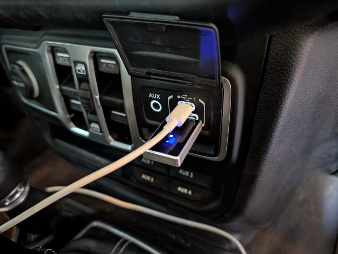 A close-up of a USB dongle plugged into a car's USB port, with a white charging cable attached.