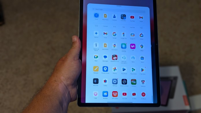 A person holding a Lenovo tablet displaying various app icons on the screen.