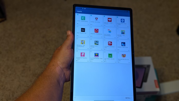 A person holding a large tablet displaying an app selection screen, showcasing various applications and their icons.