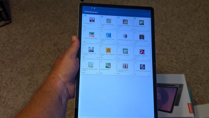 A person holding a Lenovo tablet displaying various app icons in the 'Entertainment' section, showcasing a selection of games and puzzles.