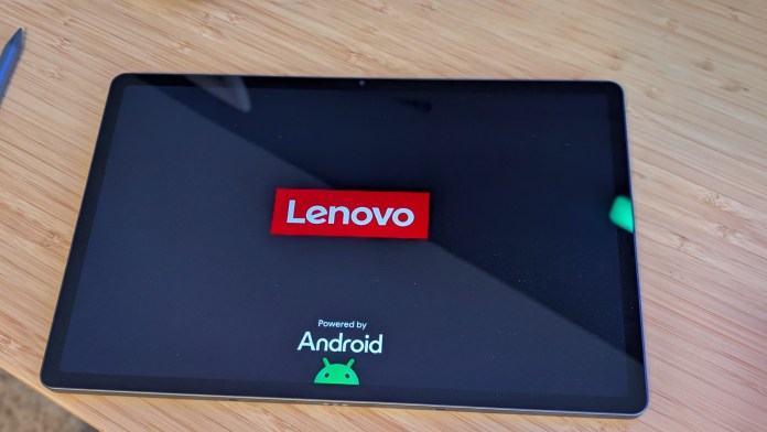 A Lenovo tablet displaying the logo on a wooden surface, with a stylus pen nearby.