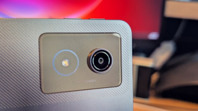 Close-up of the rear camera of a Lenovo tablet, featuring a round camera lens and a button with a reflective surface, set against a blurred background.