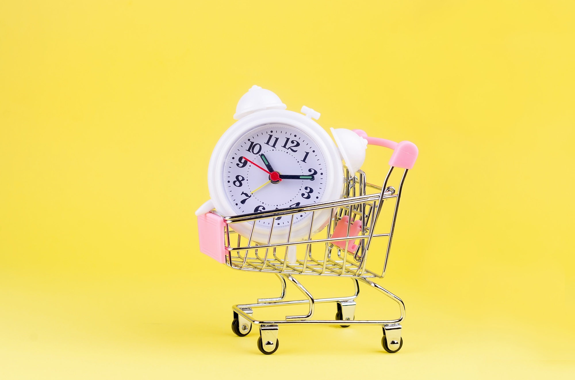 White classic alarm clock in a shopping cart isolated on yellow background