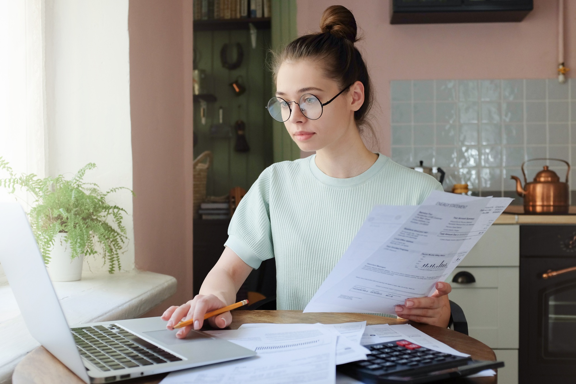 Attractive woman managing domestic budget, sitting at kitchen table with open laptop
