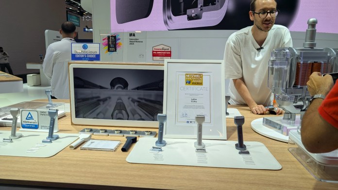 A display at IFA 2025 featuring Laifen's T1 Pro electric razor, an award certificate, and various product prototypes on a wooden table. A presenter is engaged with attendees in the background.