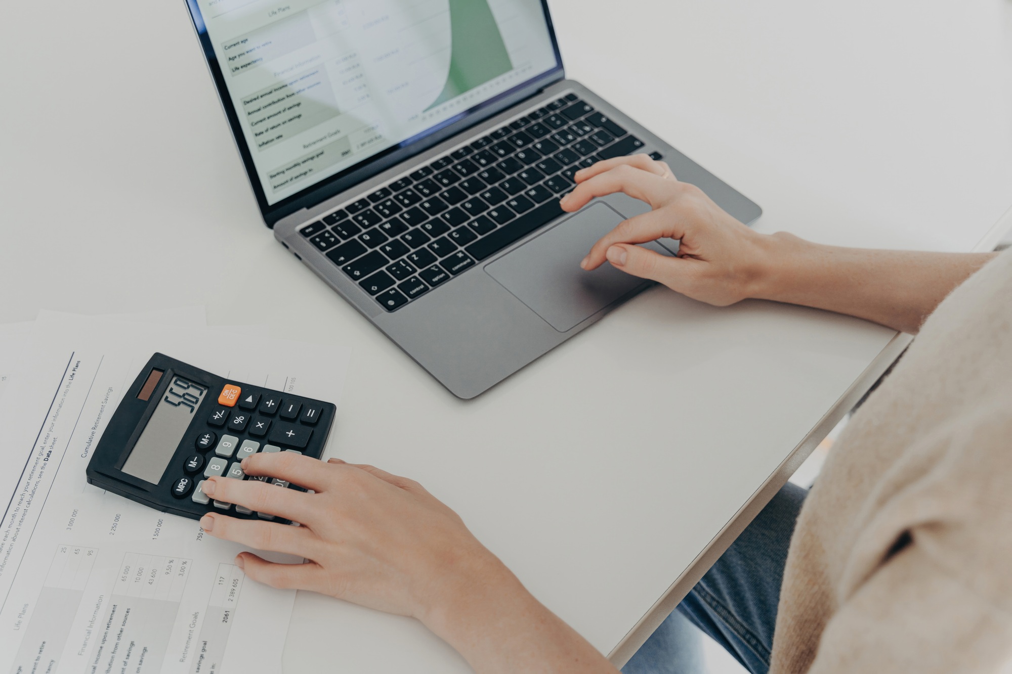 Close-up of hands using calculator and laptop on white desk, concept of finance, budgeting