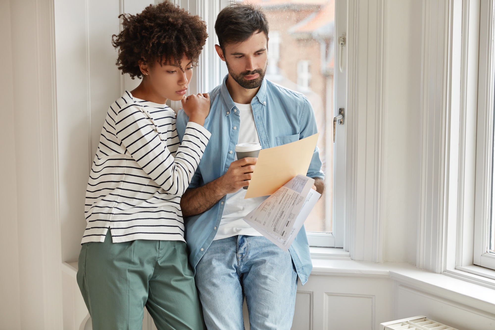 Interracial young woman and man make accounting of their expenses for year, concentrated on paper wo