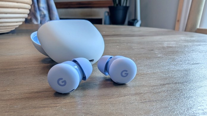 Close-up of Google Pixel Buds 2a in light blue color beside their charging case on a wooden surface.