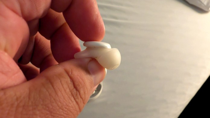 A close-up image of a hand holding a small white sleep earbud, showcasing its compact and ergonomic design.