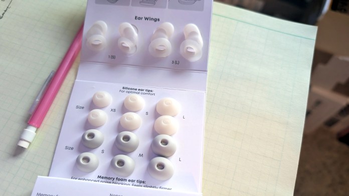 Image of the Soundcore Sleep A30 earbud tips and wings with various sizes labeled in a guide, alongside a pink pen and notebook.
