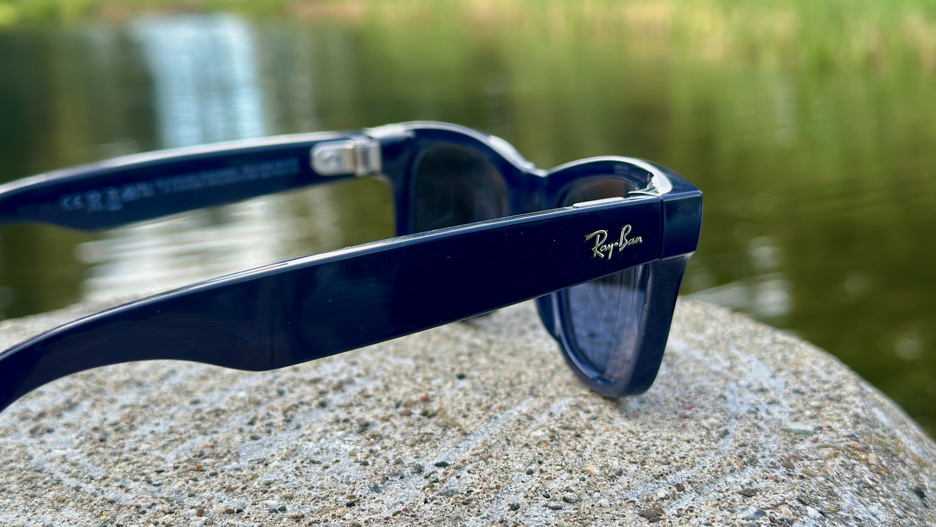 A photo of the Ray-Ban Meta (Gen 2) smart glasses sitting on a rock, angled to focus on the right arm with the Ray-Ban logo.
